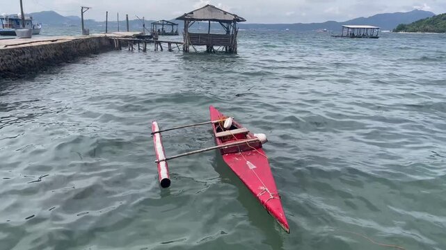 Red traditional outrigger boat floating on tropical sea near dock