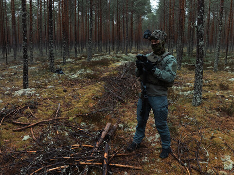 Professional drone pilot in tactical gear operating a remote controller for aerial reconnaissance during a military mission in a dense forest