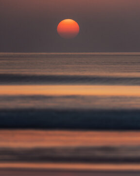 View of the large orange sun setting over the calm ocean waves with a soft purple sky in Balochistan, Pakistan.