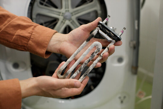 Hands holding washing machine heating element showing limescale damage