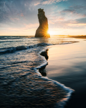 View of the Princess of Hope rock formation on the sandy shore with ocean waves and a sunburst at sunset in Balochistan, Pakistan.