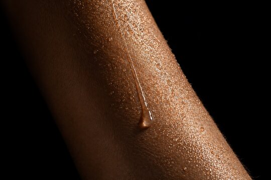 Close-up macro shot of a single drop of sweat trickling down a person's arm against a black background.