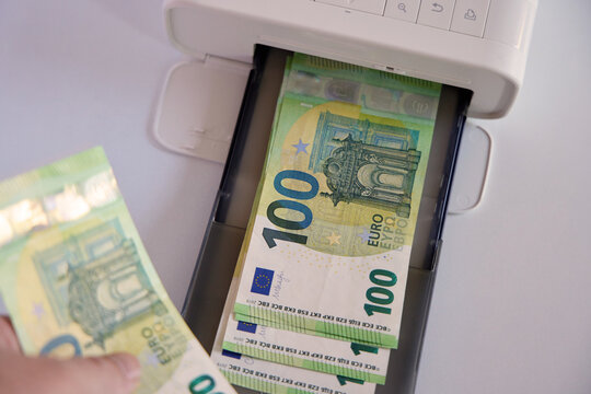 Person holding a 100 Euro banknote next to a printer tray full of cash. Concept of illegal money production, counterfeit currency, or high income.