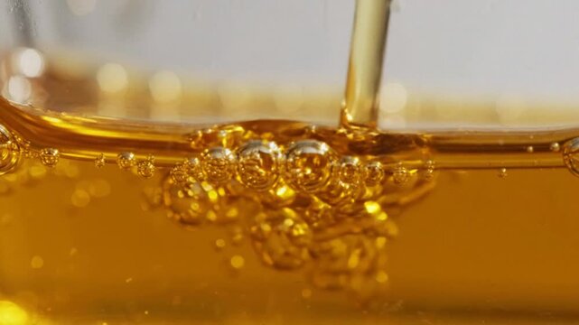 Macro shot of golden cosmetic serum oil pouring with bubbles for a luxurious hydrating treatment.