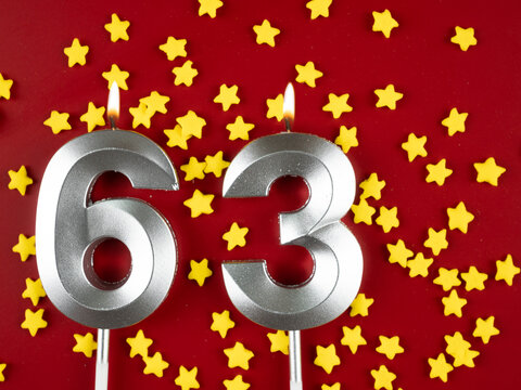 Number 63 silver celebration birthday candle on red with golden stars background. Sixty-three years birthday. celebrating anniversary and birthday