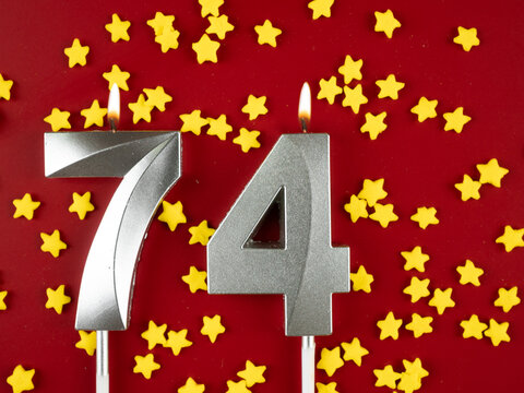 Number 74 silver celebration birthday candle on red with golden stars background. Seventy-four years birthday. celebrating anniversary and birthday