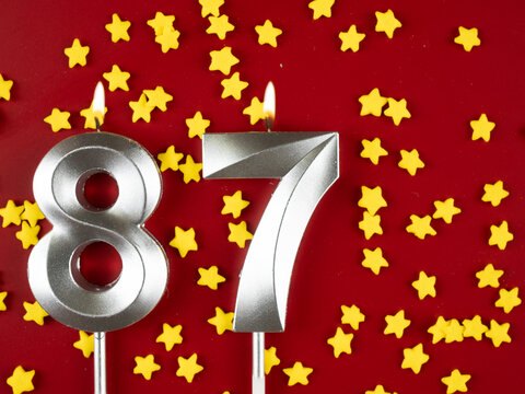Number 87 silver celebration birthday candle on red with golden stars background. Eighty-seven years birthday. celebrating anniversary and birthday