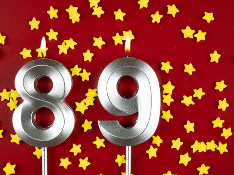 Number 89 silver celebration birthday candle on red with golden stars background. Eighty-nine years birthday. celebrating anniversary and birthday