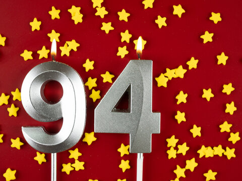 Number 94 silver celebration birthday candle on red with golden stars background. Ninety-four years birthday. celebrating anniversary and birthday