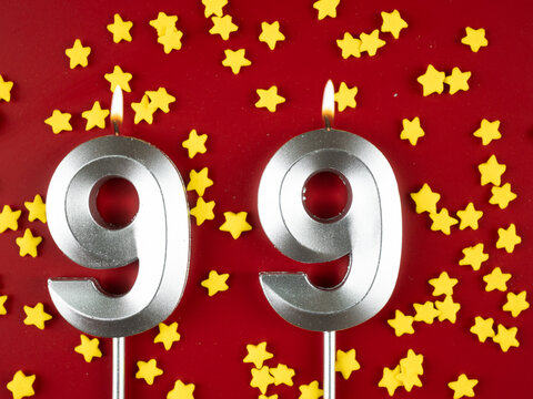 Number 99 silver celebration birthday candle on red with golden stars background. Ninety-nine years birthday. celebrating anniversary and birthday