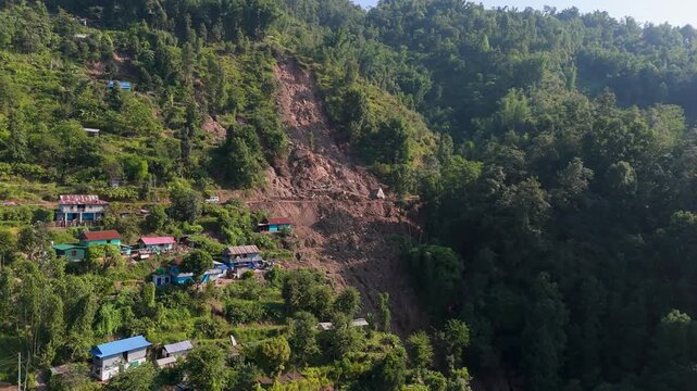 Aerial High Angle View of a Significant Landslide Scar Near a Rural Mountain Village on Lush Slopes