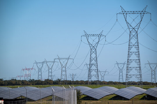View of high-voltage electricity pylons and rows of solar panels under a clear blue sky in Palmela, Setubal, Portugal.