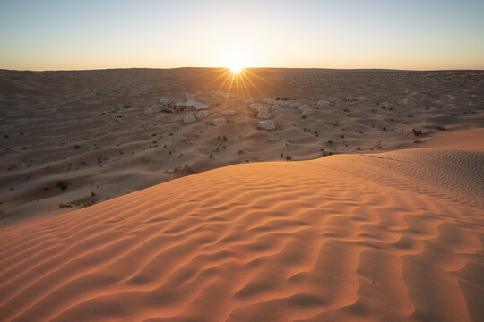 View of a desert camp with white tents nestled among sand dunes under a golden sunrise in Kebili, Kebili Governorate, Tunisia.