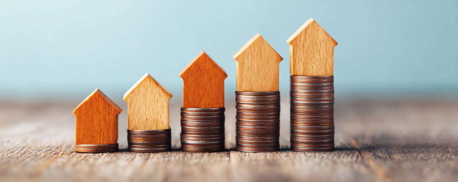 Rising stack of wooden house models on coins representing growing real estate market value and long term property investment success
