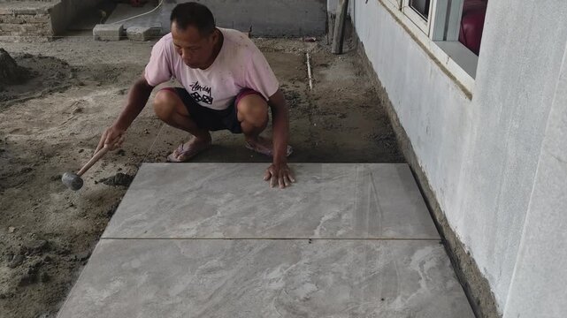 Construction worker tapping granite floor tile with a rubber mallet to level the surface during floor installation. Precision tiling work.