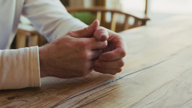A person nervously cracking fingers while waiting sitting at the table