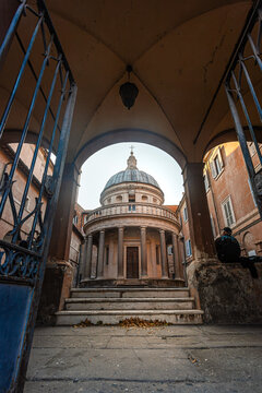 The Tempietto of San Pietro in Montorio by Donato Bramante in Rome. A masterpiece of High Renaissance architecture framed by a historic archway and gate.