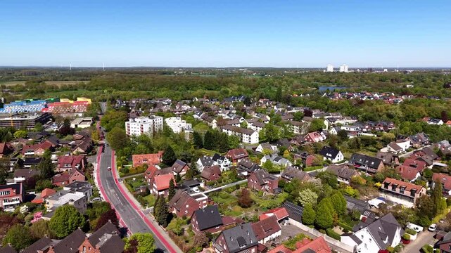 Aerial view of calm German residential district in spring, with single family homes, red brick houses, tree-lined streets and sunny skies with city skyline in distance. Wide shot.