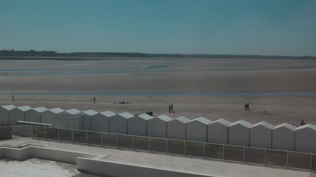 High angle view of the beach huts and shoreline at Le Crotoy, France, with people walking along the bay at low tide.