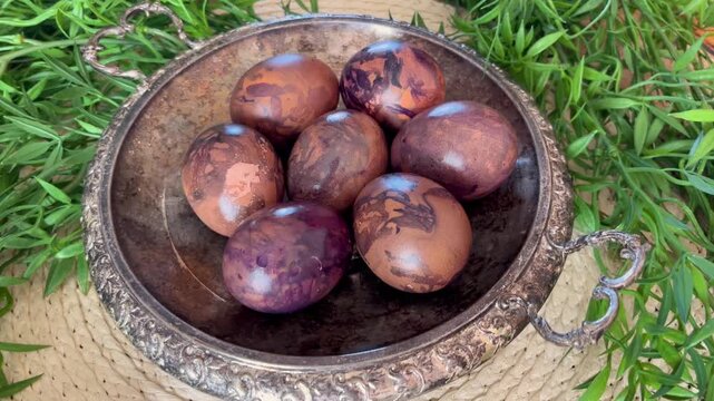 Naturally dyed Easter eggs in an antique metal bowl with fresh greenery, styled as a rustic spring holiday centerpiece on a woven table mat.