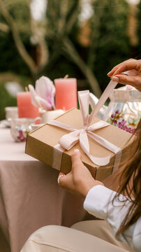 Woman's hands carefully untying a ribbon on a gift box during an outdoor garden party