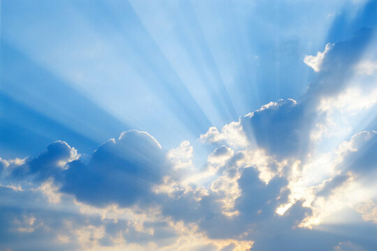 Dramatic sky with sun rays shining through fluffy white clouds