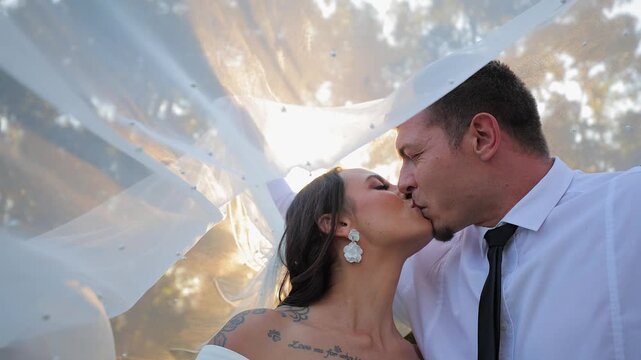 Bride and groom kiss at wedding under diffuse light under lacy veil