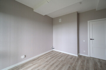 Obraz premium clean, empty room with light grey walls, wooden laminate flooring, white ceiling, one white interior door, minimal fixtures, neutral tones, ready for furnishing