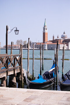 View of traditional gondolas moored at a wooden pier with the San Giorgio Maggiore church across the lagoon in Venice, Veneto, Italy.