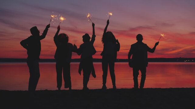 Silhouette of Cheerful People Raising Arms and Dancing at Sunset, Symbol of Freedom and Achievement