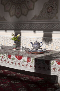 View of a traditional ceramic tea set and a vase of flowers on an embroidered tablecloth in an ornate room in Tashkent, Uzbekistan.