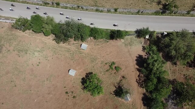 Drone shot of cyclists in a peloton competing in the 'Vuelta a Mallorca' 2026; scenic country road surrounded by trees and traditional stone walls.