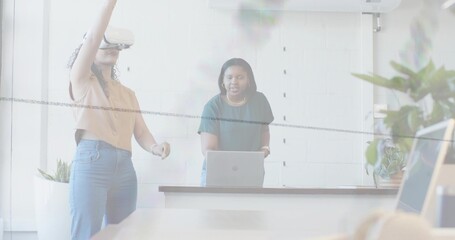 Obraz premium Interacting two women wearing VR headset and tee, testing on laptop at long conference table