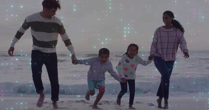 Running family of four holding hands on wet sand at beach, wearing sweaters, teal pink speckles