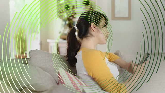 Woman sitting sofa tapping phone starting green rings growing around her as viewing tech content