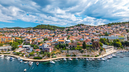 Obraz premium Aerial view of a coastal town in Croatia with red roof houses on a hillside overlooking the blue Adriatic sea and harbor with boats