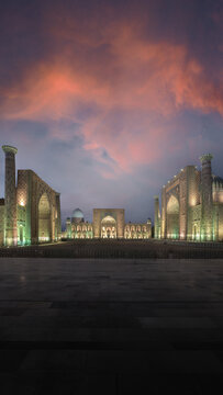 View of Registan Square with illuminated madrasahs under a dramatic sunset sky in Samarkand, Samarqand Region, Uzbekistan.