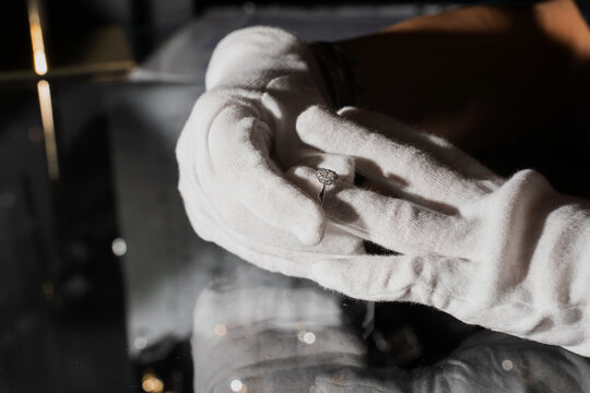Close up of gloved hands inspecting silver gemstone ring in workshop.