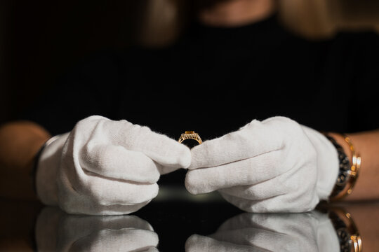 Professional examining silver gemstone ring with gloves in workshop.
