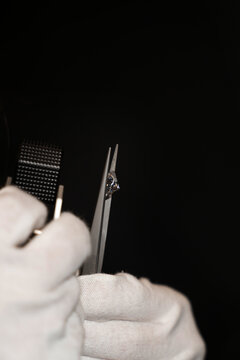 Gemologist inspects a diamond using tweezers and a loupe to evaluate clarity and cut quality.