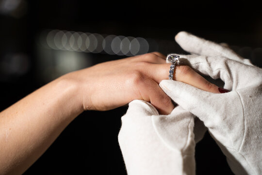 Jeweler placing engagement ring on bride finger during purchase in boutique.