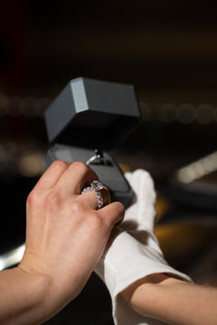 Bride trying on ring while jeweler adjusts fit in retail store environment.