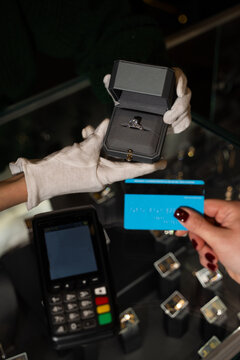 Bride holding payment card while buying engagement ring in store.