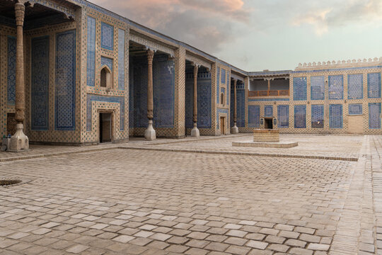 View of the ornate courtyard with blue mosaic tiles and carved wooden columns in Khiva, Xorazm Region, Uzbekistan.