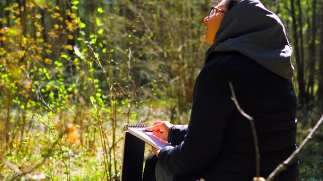 Woman Drawing in Sketchbook Outdoors Seen from Behind with Glowing Spring Forest in Background | Creative Flow in Nature, Where the Best Ideas Come to Life