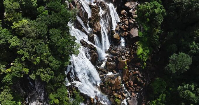 Cinematic aerial 4K footage of Veu da Noiva waterfall located in the Serra do Mar, Brazil. The scene showcases powerful cascading water flowing over rocky cliffs surrounded by dense tropical rainfores