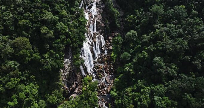 Cinematic aerial 4K footage of Veu da Noiva waterfall located in the Serra do Mar, Brazil. The scene showcases powerful cascading water flowing over rocky cliffs surrounded by dense tropical rainfores