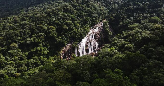Cinematic aerial 4K footage of Veu da Noiva waterfall located in the Serra do Mar, Brazil. The scene showcases powerful cascading water flowing over rocky cliffs surrounded by dense tropical rainfores