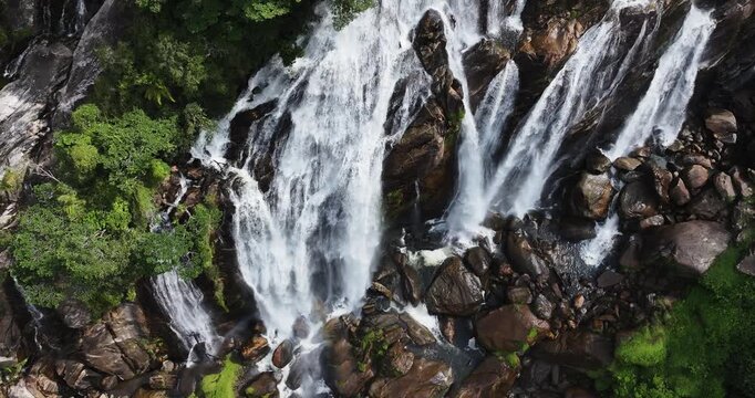Cinematic aerial 4K footage of Veu da Noiva waterfall located in the Serra do Mar, Brazil. The scene showcases powerful cascading water flowing over rocky cliffs surrounded by dense tropical rainfores