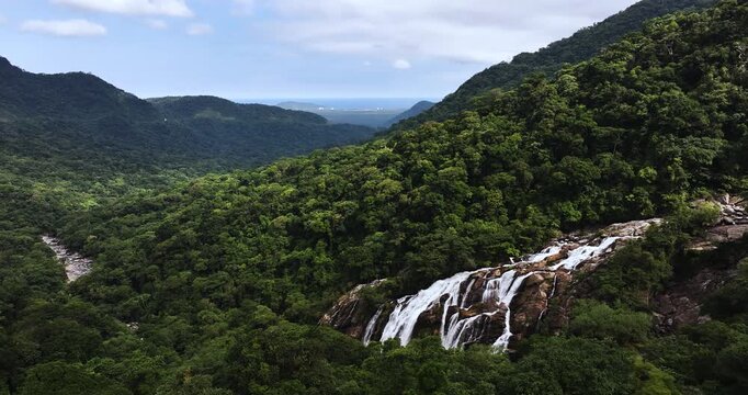 Cinematic aerial 4K footage of Veu da Noiva waterfall located in the Serra do Mar, Brazil. The scene showcases powerful cascading water flowing over rocky cliffs surrounded by dense tropical rainfores